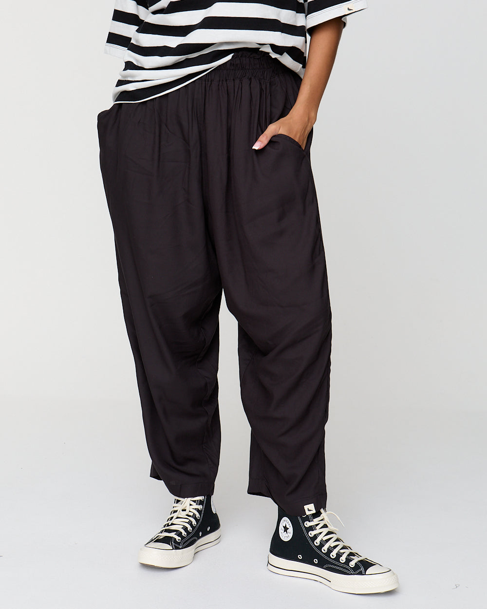 Person wearing black high-waisted pants and black Converse shoes on a white background