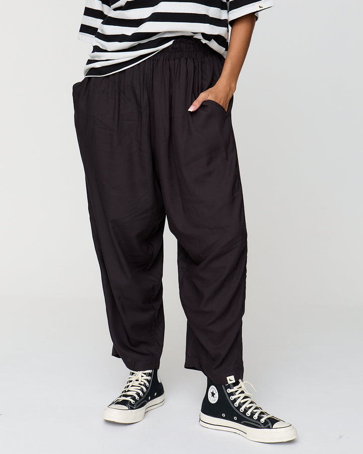 Person wearing black high-waisted pants and black Converse shoes on a white background