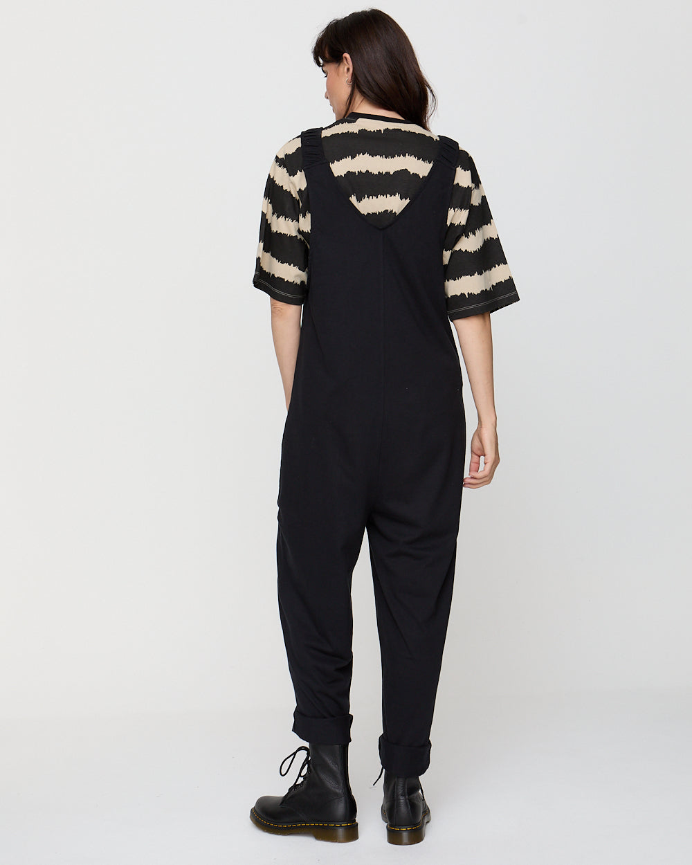 Person wearing black overalls with a striped shirt on a white background