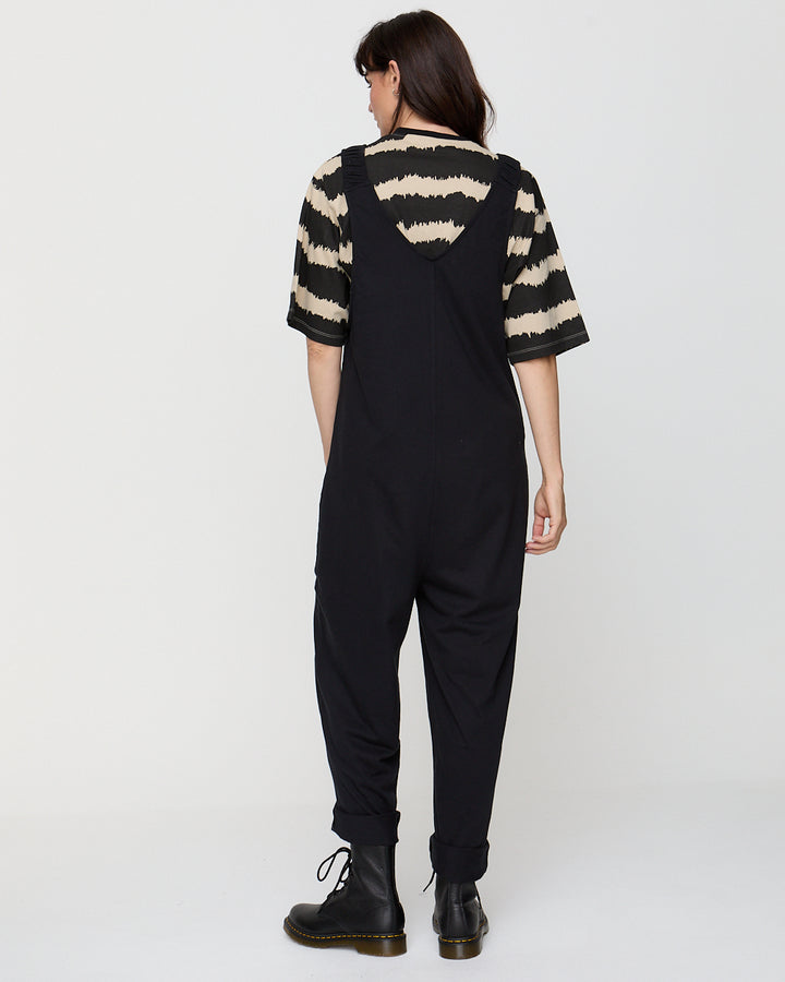 Person wearing black overalls with a striped shirt on a white background
