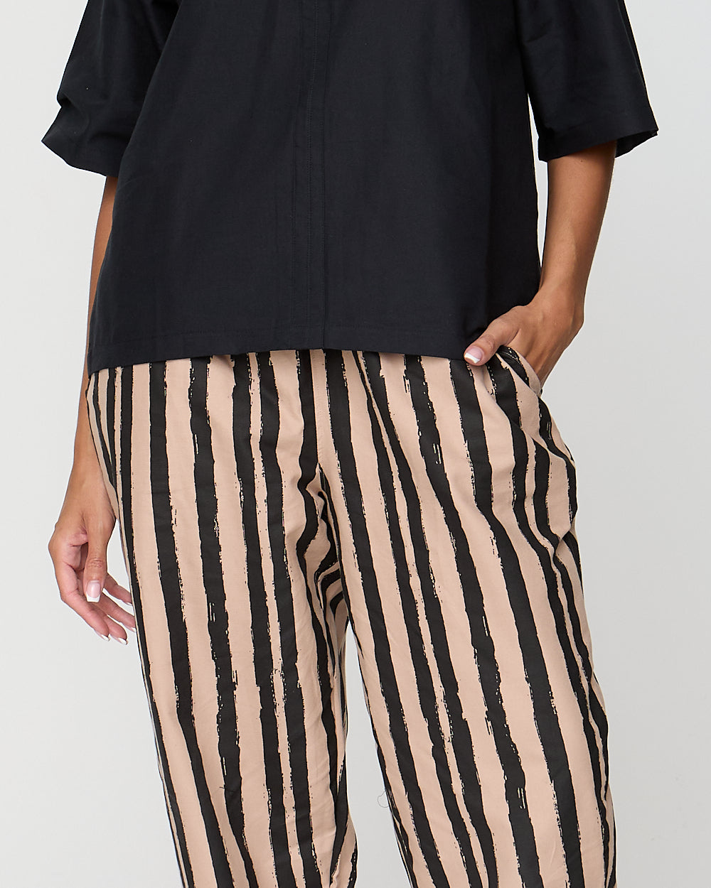 Person wearing black top and beige and black striped pants on a plain background
