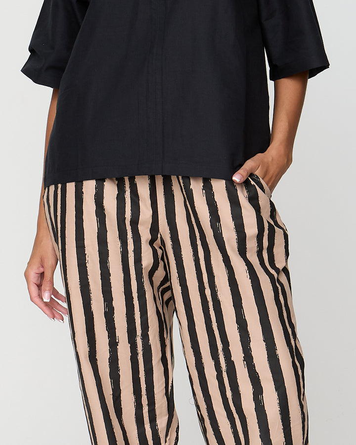 Person wearing black top and beige and black striped pants on a plain background
