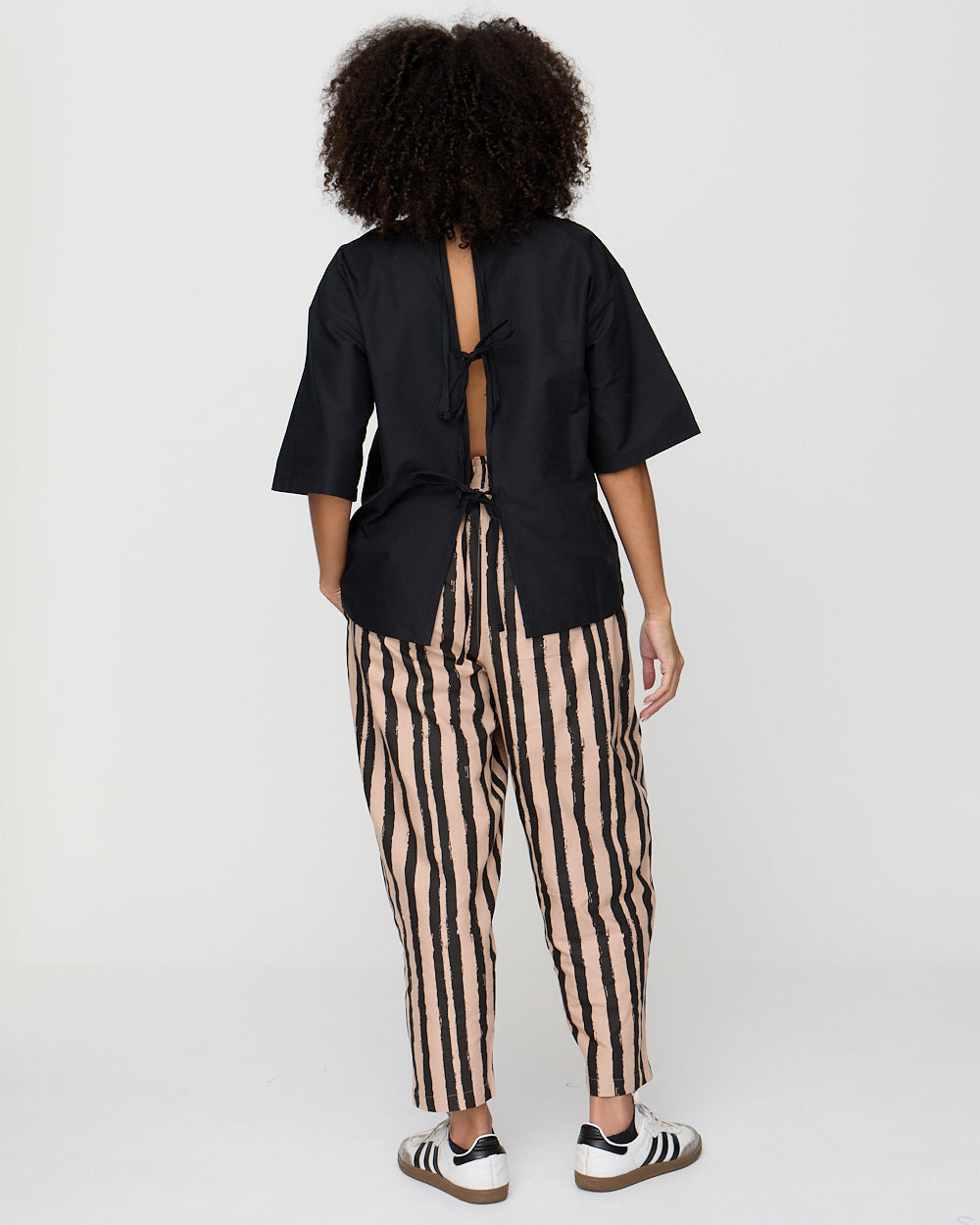 Person wearing a black top with open back and striped pants on a white background