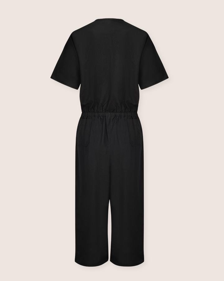 The Ethel Twill Black Jumpsuit, crafted from organic cotton, showcases an elastic waistband and wide-leg style, displayed from the back on a plain light pink background.