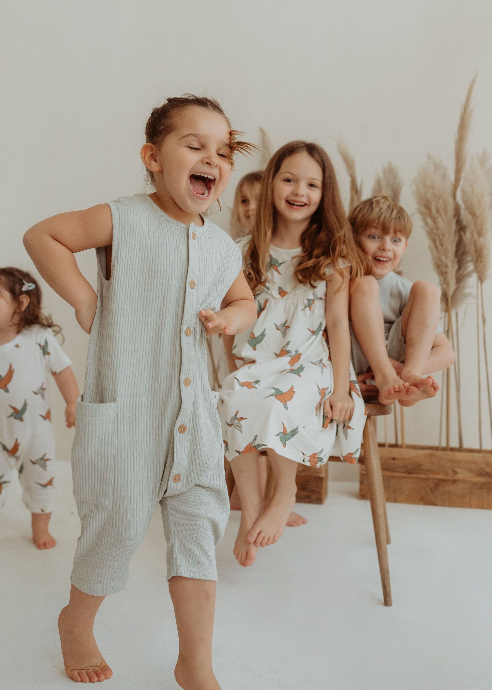 5 children laughing and playing with pampas grass in the background. wearing turtle dove kids organic kids collection. 