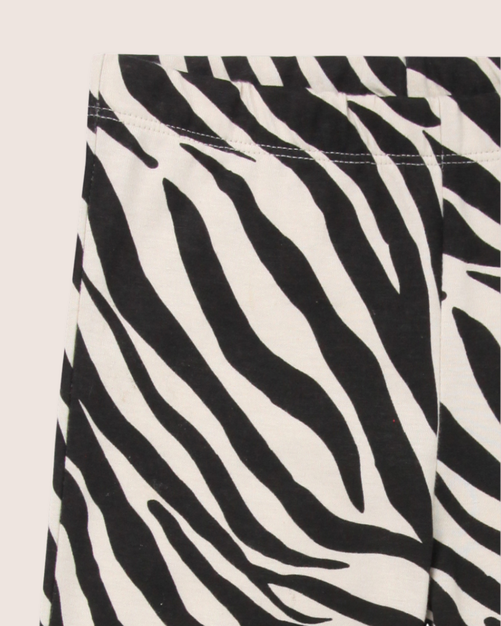 Close-up of Zebra Skin Leggings featuring a black and white pattern, highlighting the upper section with a visible waistband and vertical seam against a light-colored, plain background.