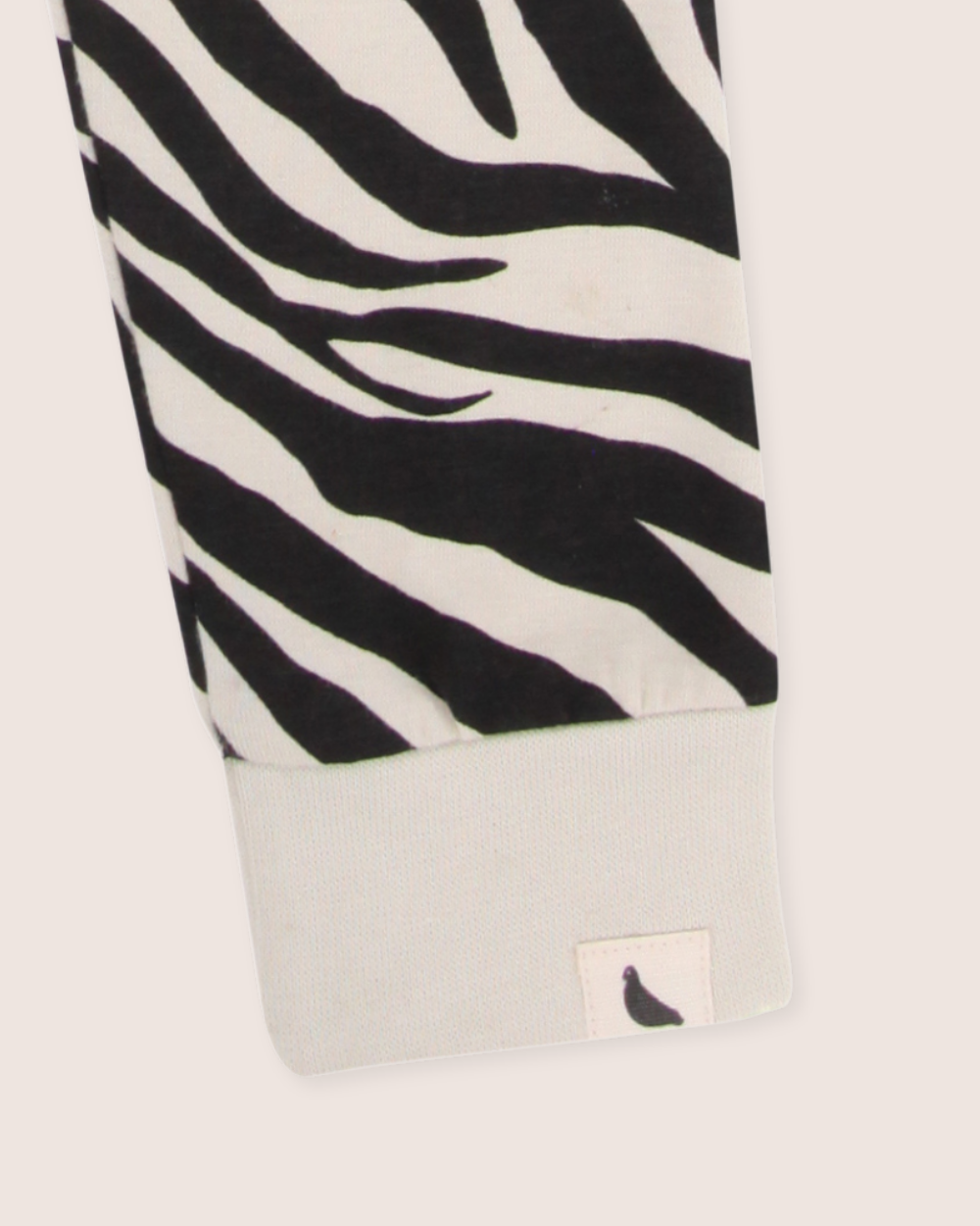 A close-up of Zebra Skin Leggings fabric showcases black and white zebra print with a cuff crafted from organic cotton. A small tag features a black bird silhouette, highlighting the charm of kids sustainable fashion.