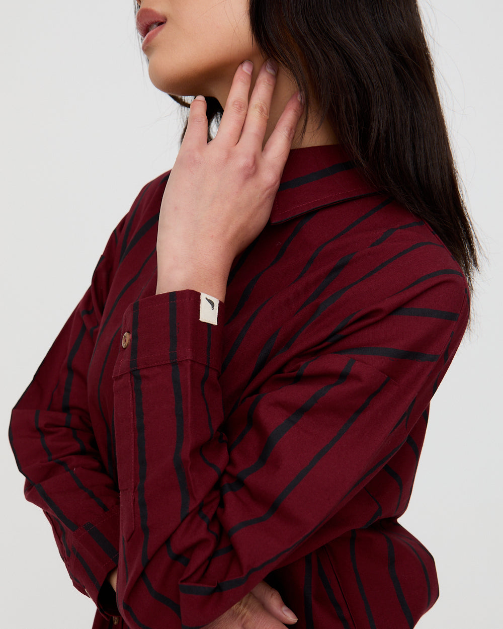 Close-up of a person wearing a burgundy shirt with black stripes against a white background