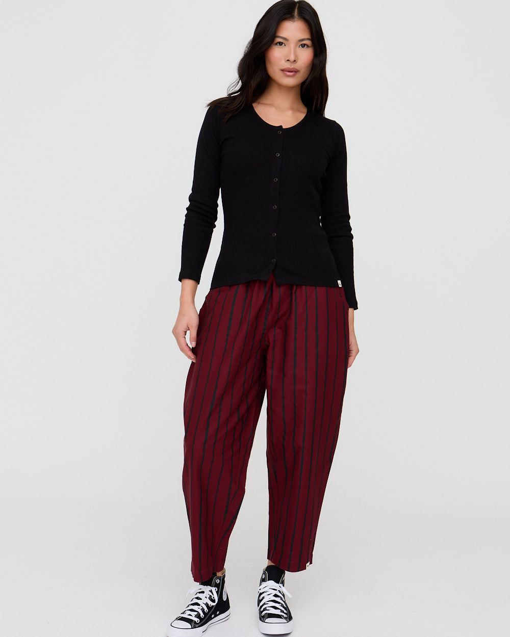 Woman wearing a black top and maroon striped pants on a white background