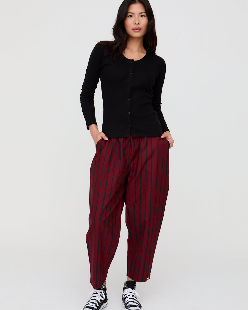 Woman wearing a black cardigan and maroon striped pants on a white background