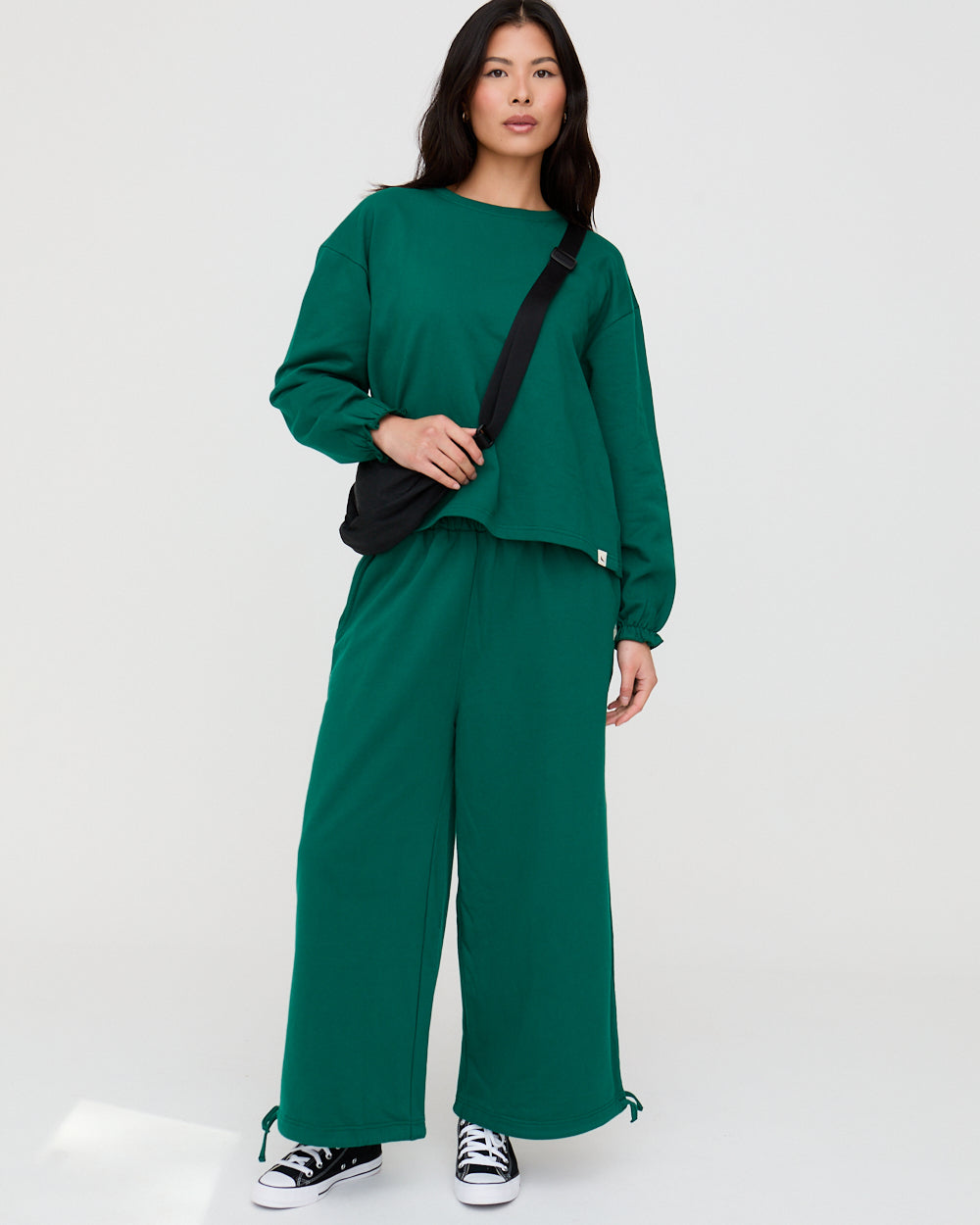 Woman wearing a green outfit with wide-leg pants and a black bag on a white background