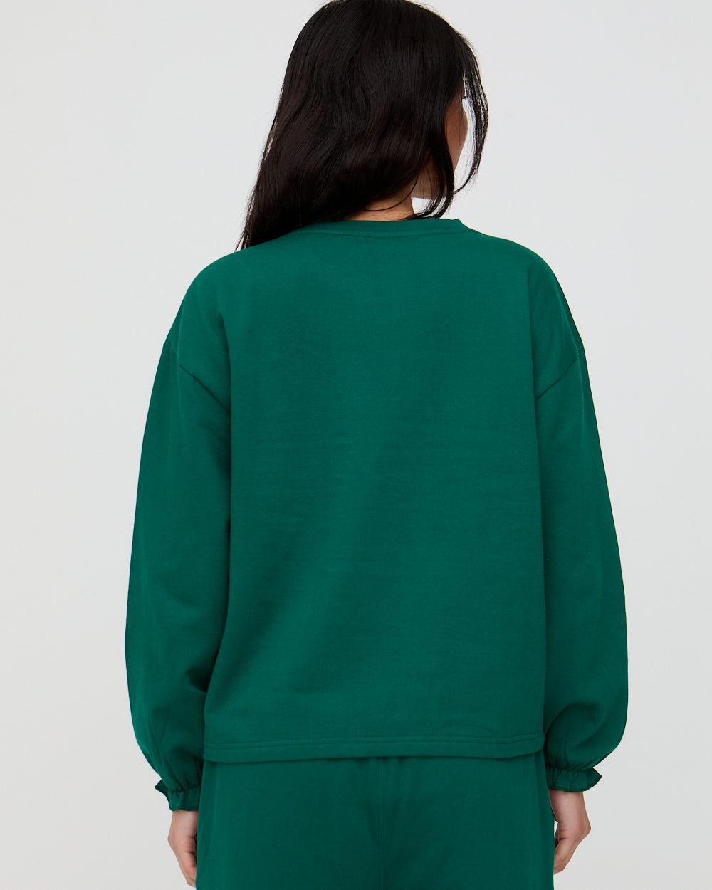 Person wearing a green sweatshirt and pants on a plain background