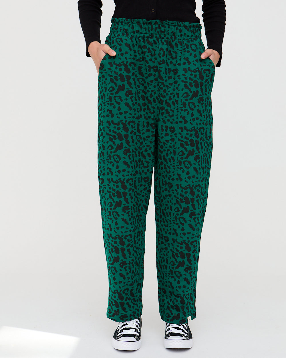 Green leopard print pants worn by a person on a white background
