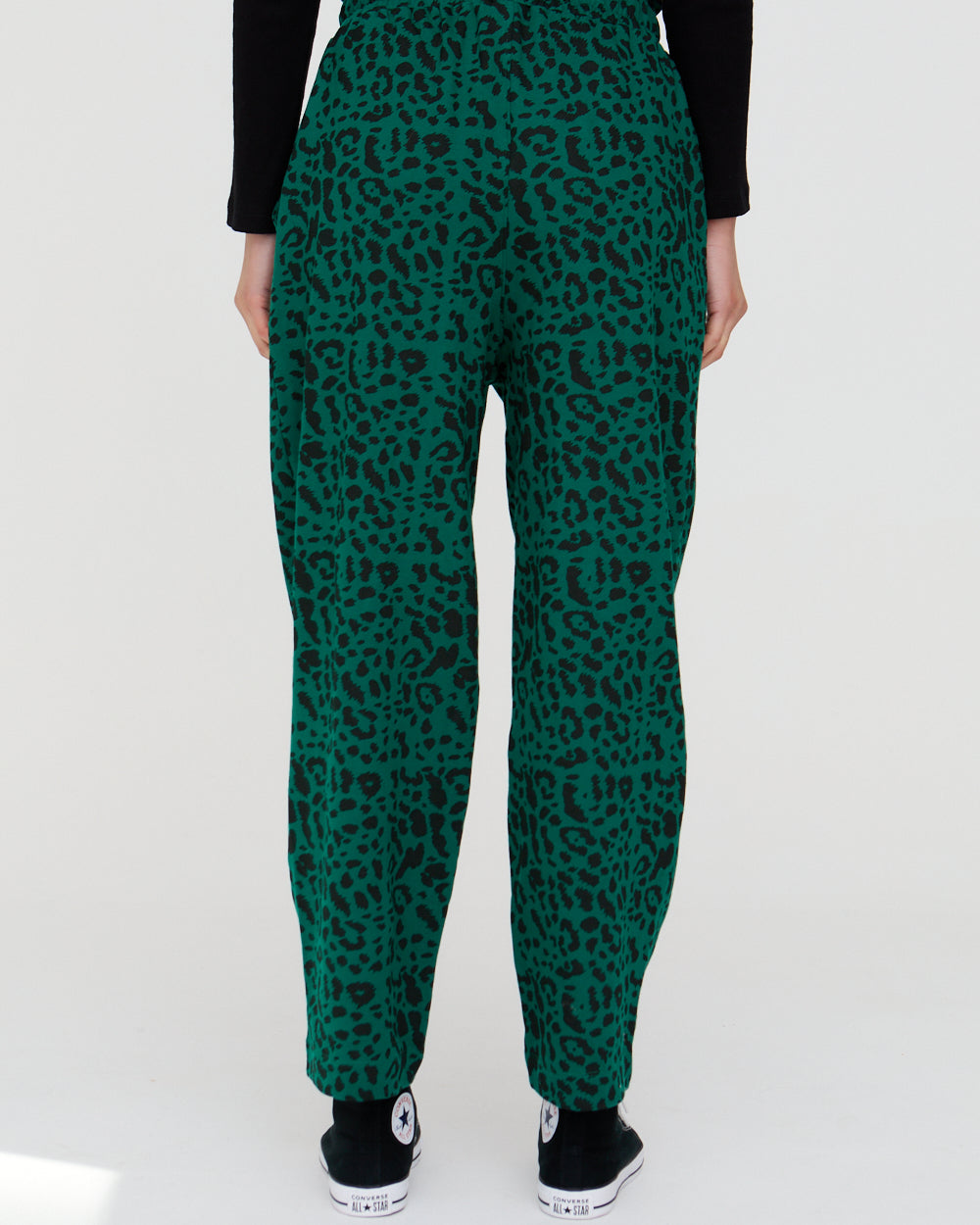 Green leopard print pants worn by a person on a white background