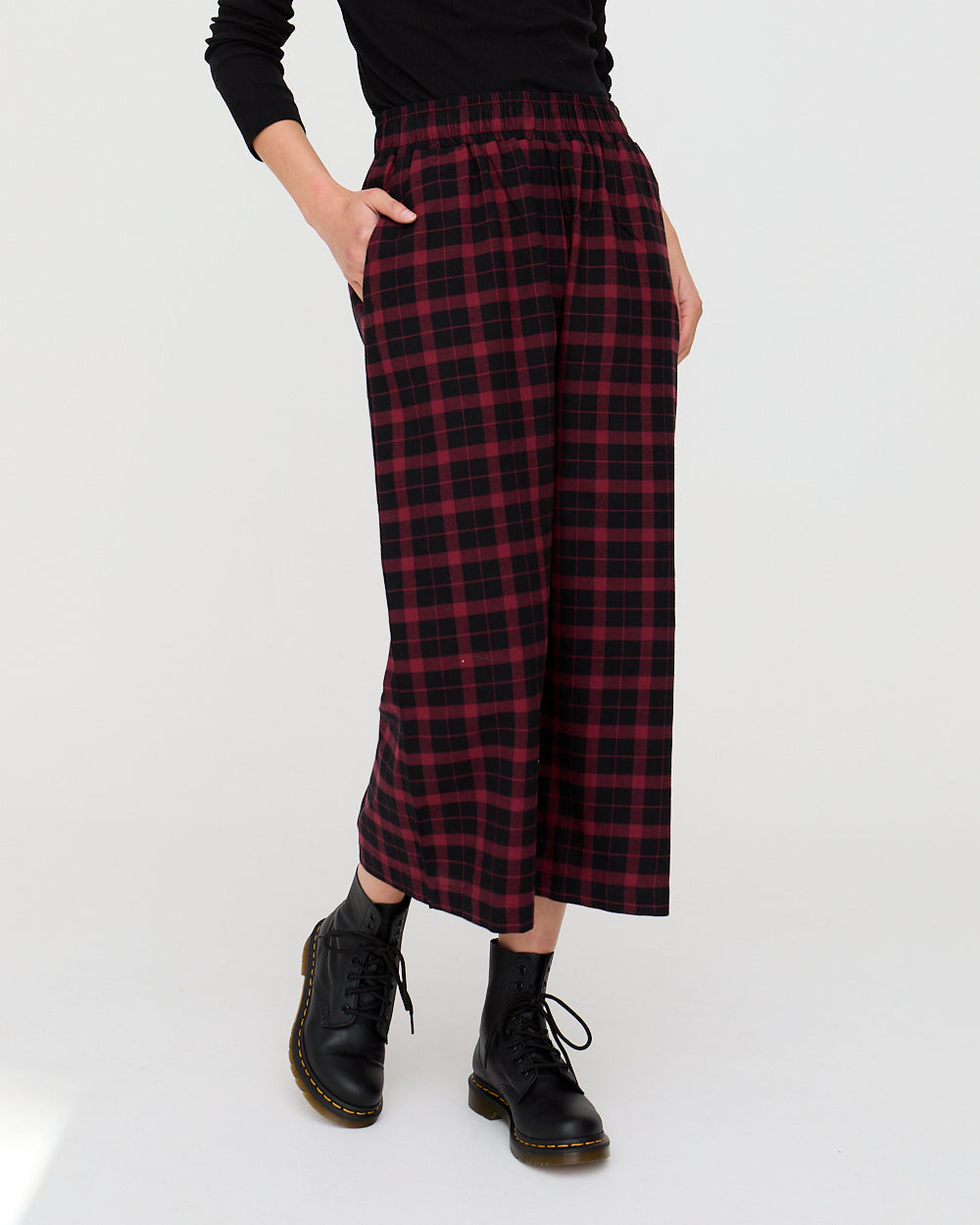 Person wearing a red and black plaid skirt with black boots on a white background