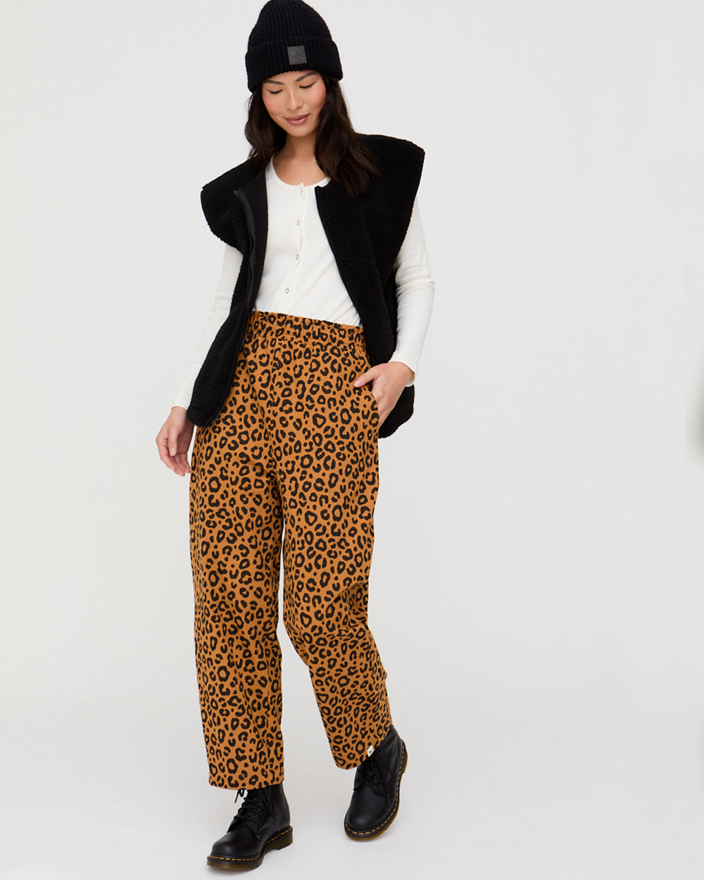 Person wearing leopard print pants with a black vest and white shirt on a white background