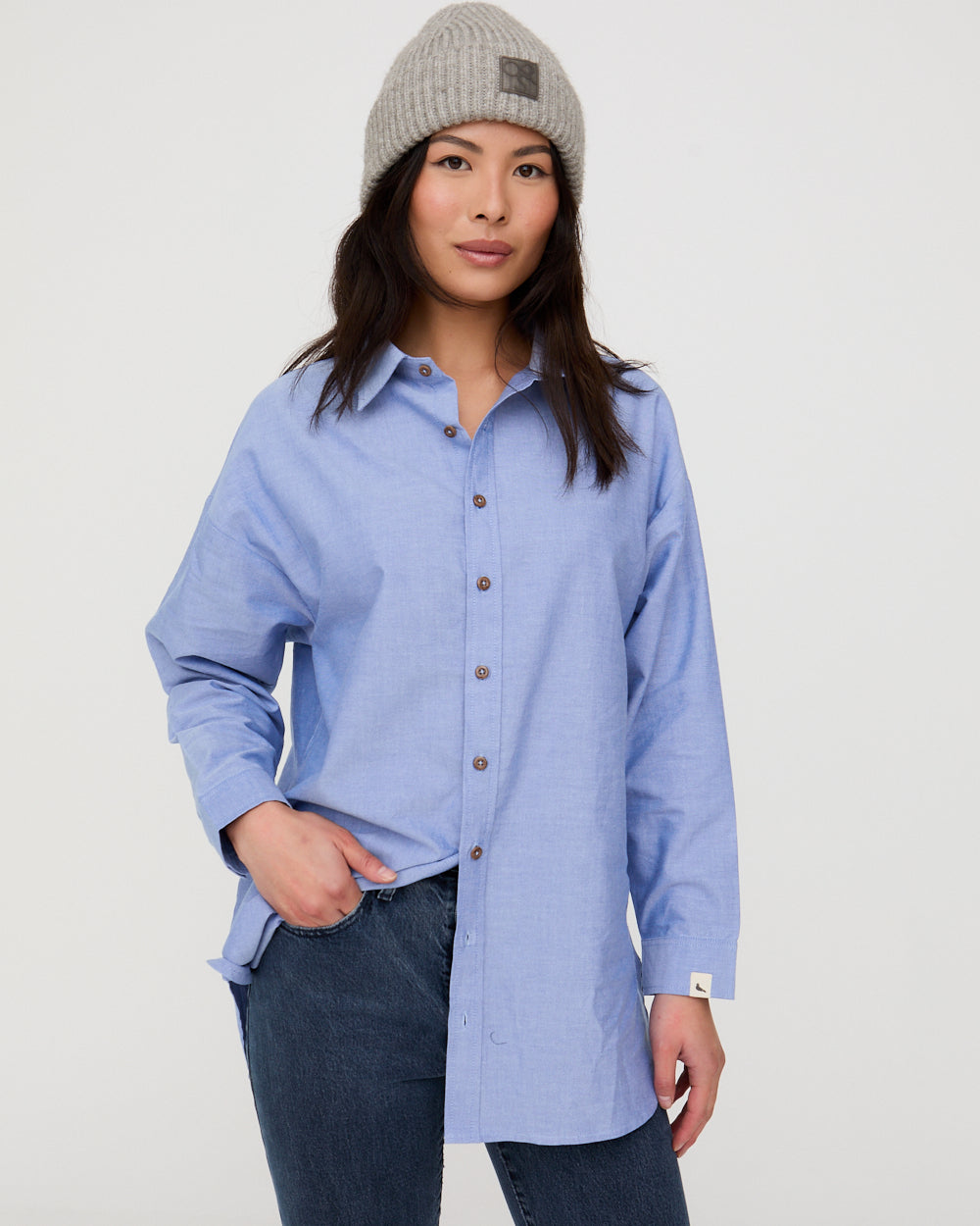 Woman wearing a light blue button-up shirt and dark jeans with a gray beanie on a white background