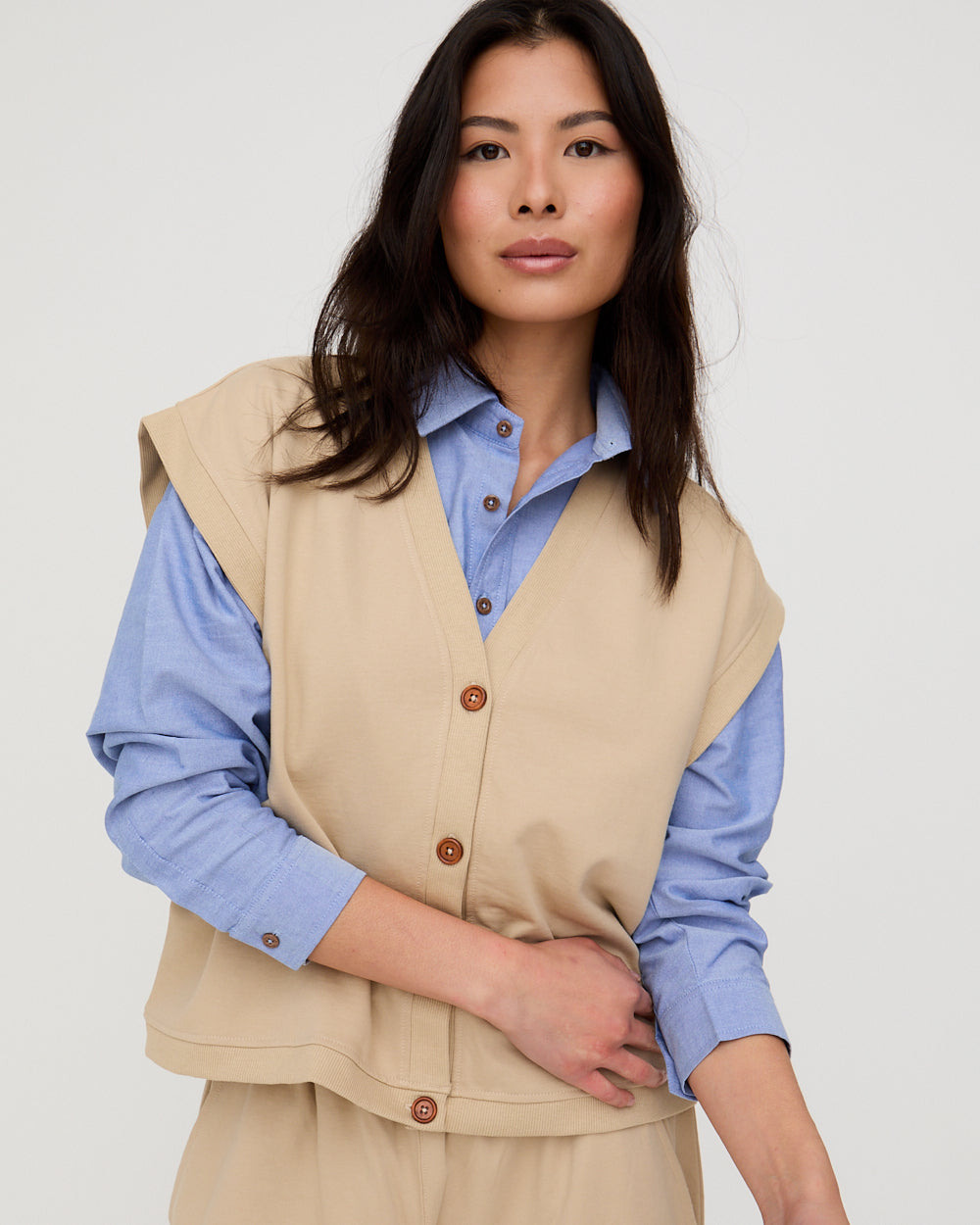 Woman wearing a beige vest over a blue shirt on a white background