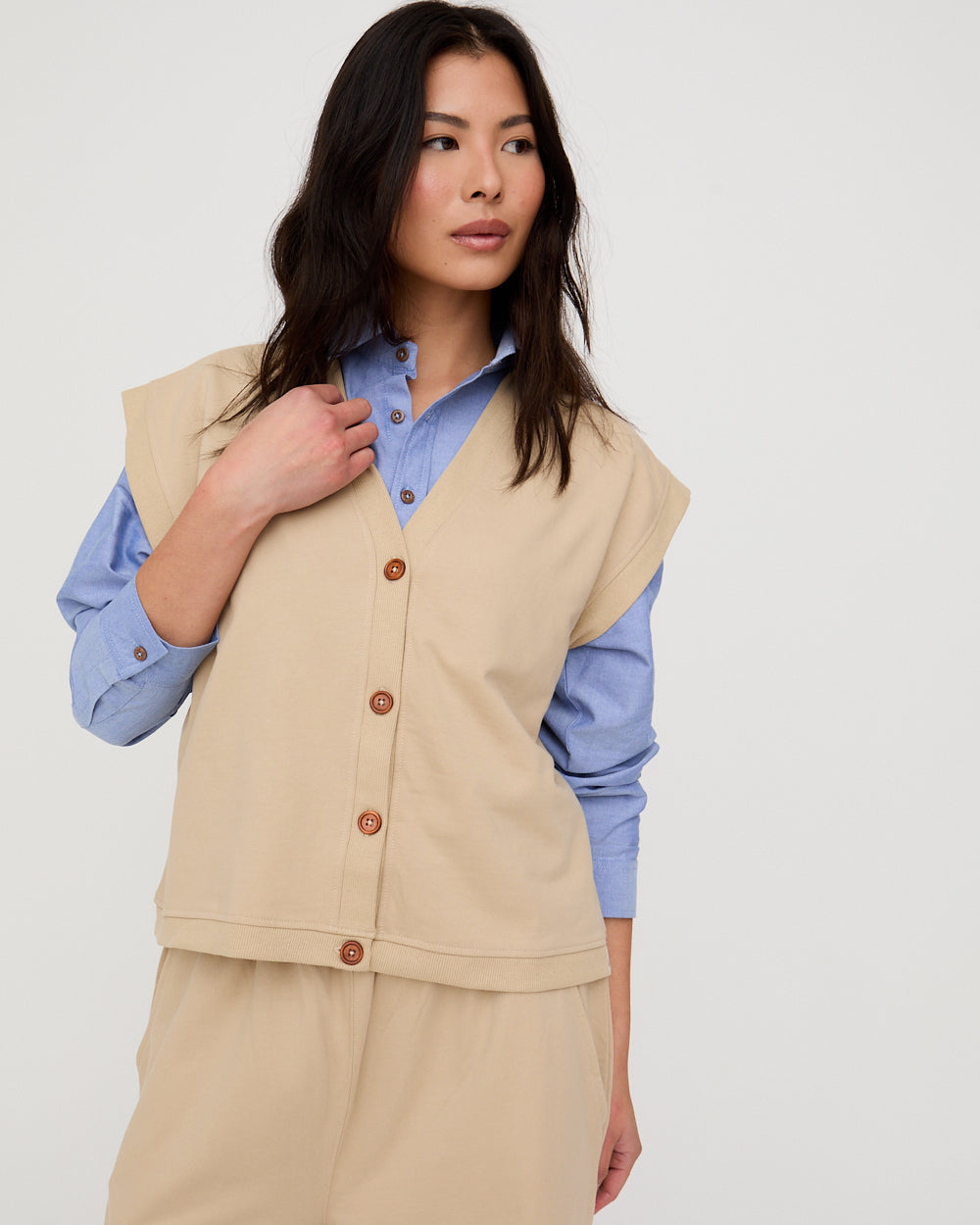 Woman wearing a beige vest over a blue shirt on a white background