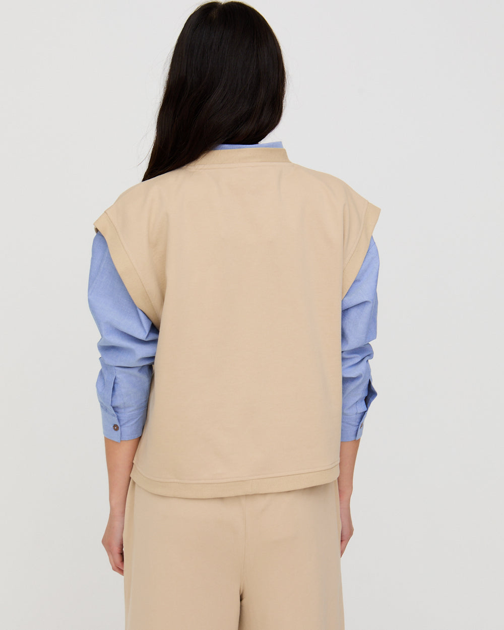 Person wearing a beige vest over a blue shirt on a plain background