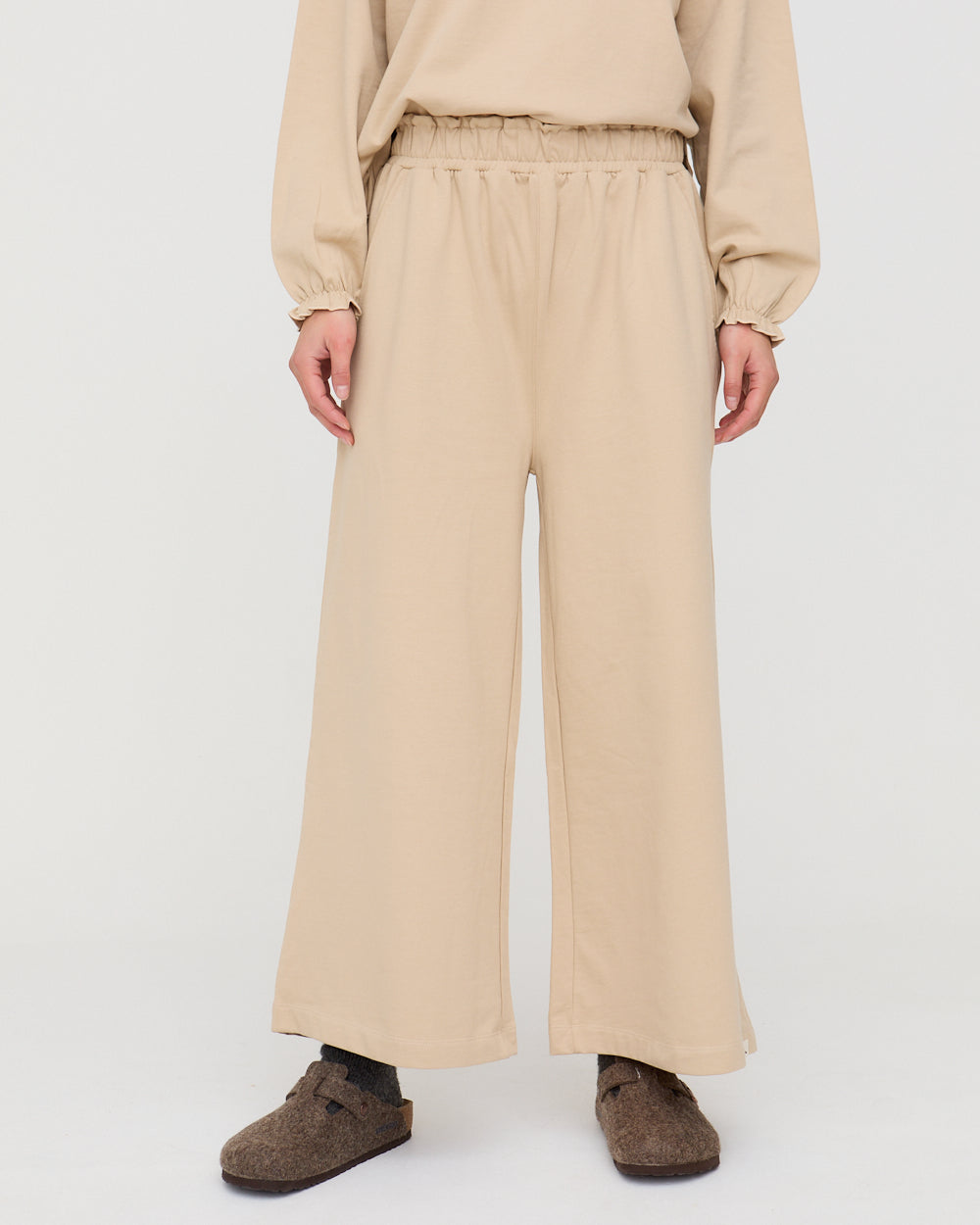Person wearing beige pants and a matching top on a white background