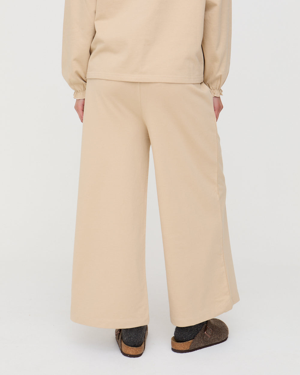 Person wearing a beige outfit with wide-leg pants on a white background