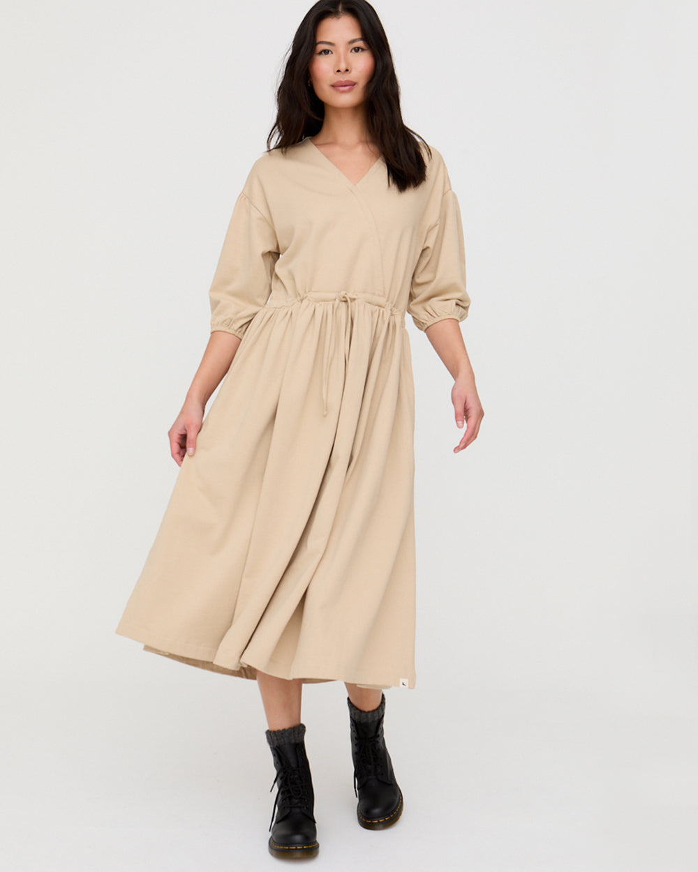 Woman wearing a beige dress with black boots on a white background