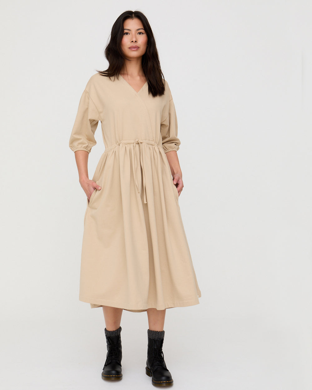 Woman wearing a beige dress with black boots on a white background