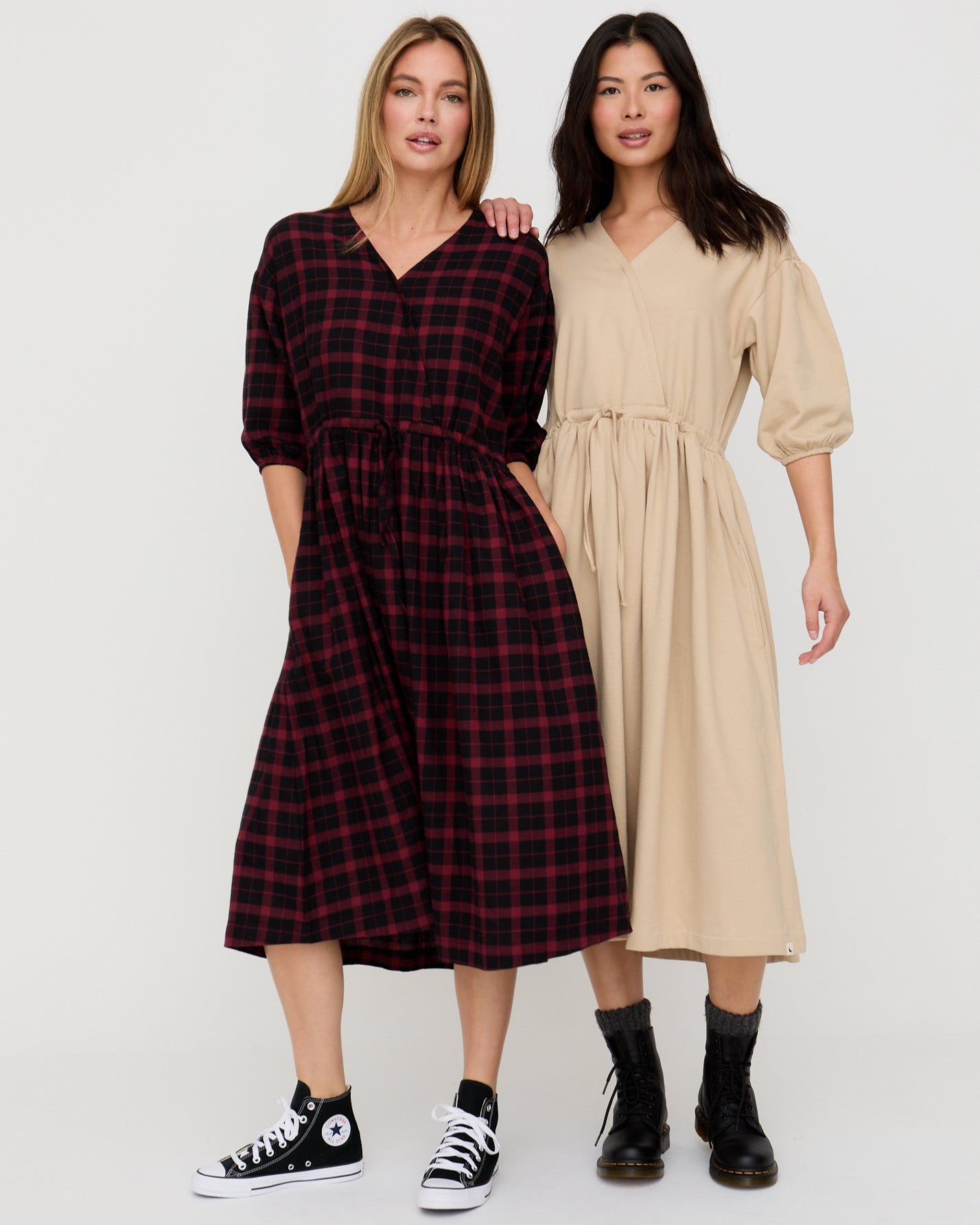 Two women wearing plaid and beige dresses standing side by side on a white background