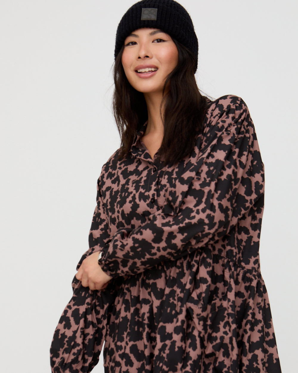 Woman wearing a leopard print dress and black beanie on a white background