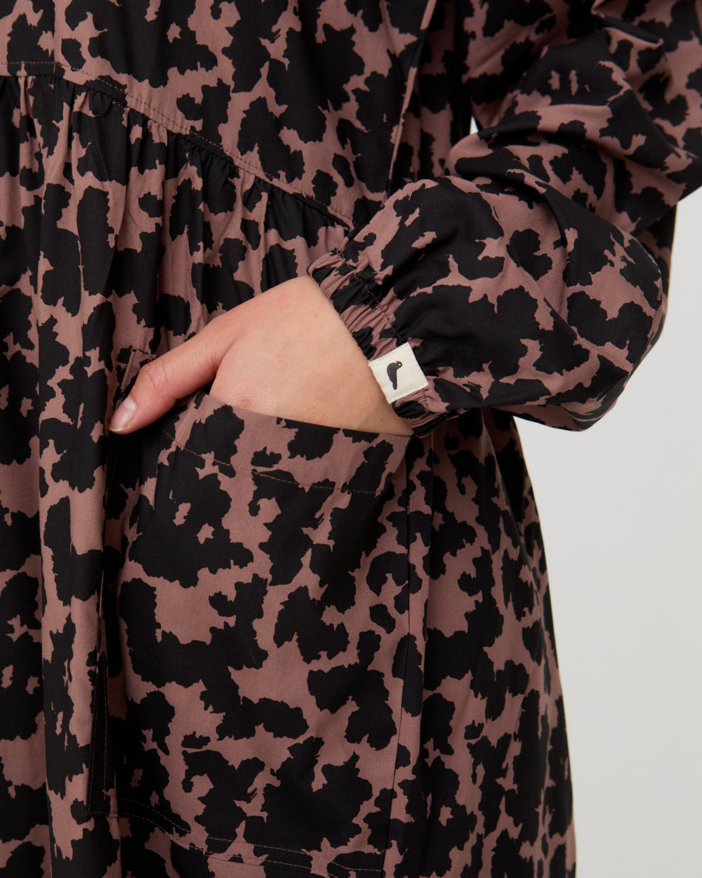 Leopard print dress with a close-up of a hand in the pocket on a light gray background