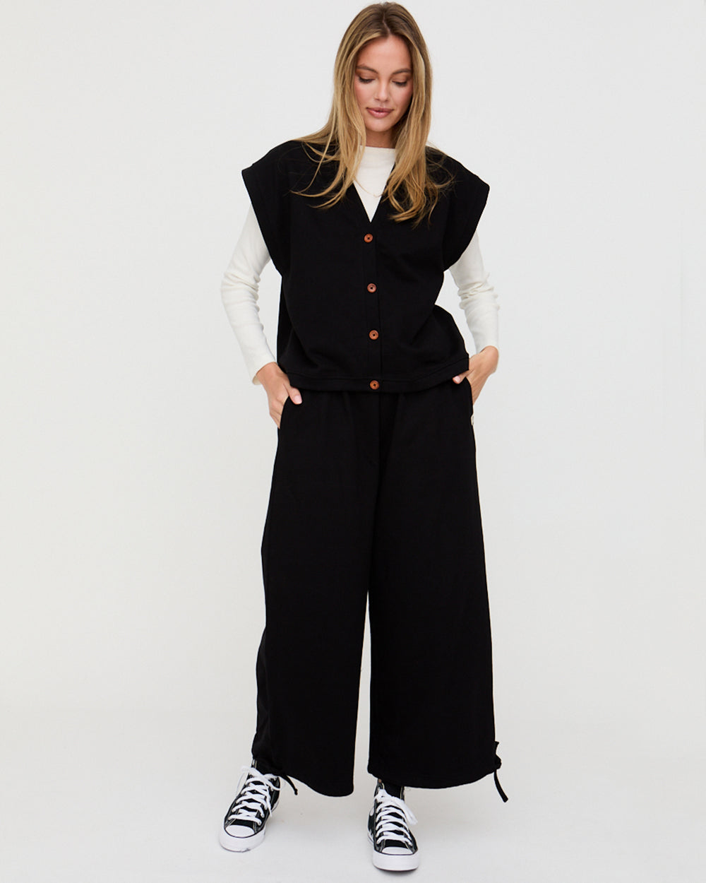 Woman wearing a black vest and wide-leg pants with a white background