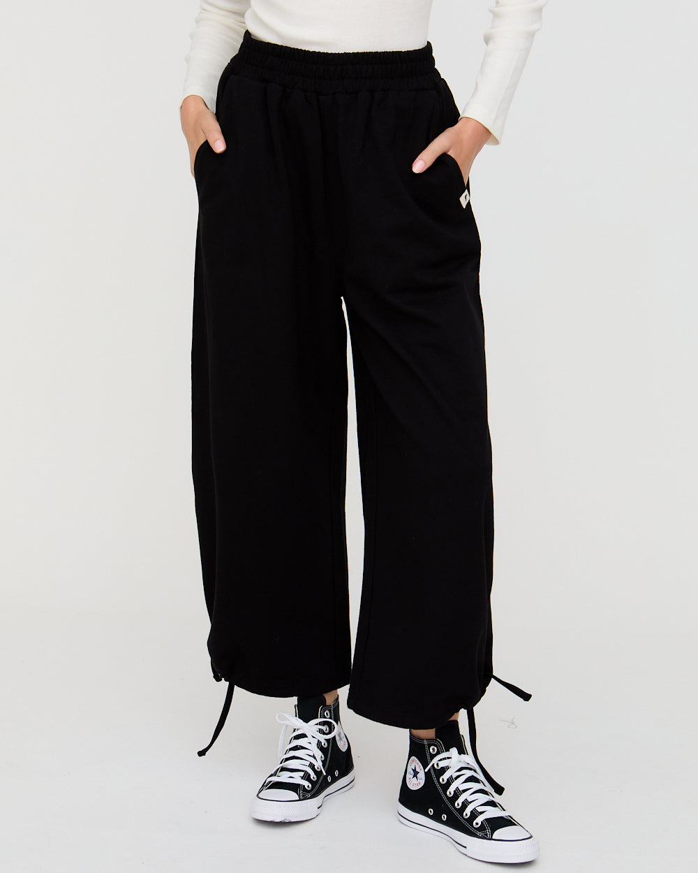 Person wearing black wide-leg pants and white sneakers on a white background