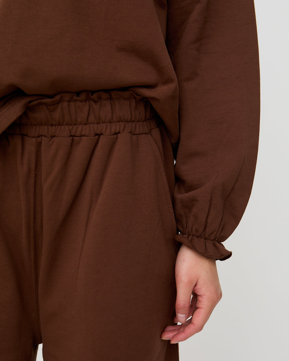 Brown outfit with a focus on the pants and long-sleeve top against a neutral background