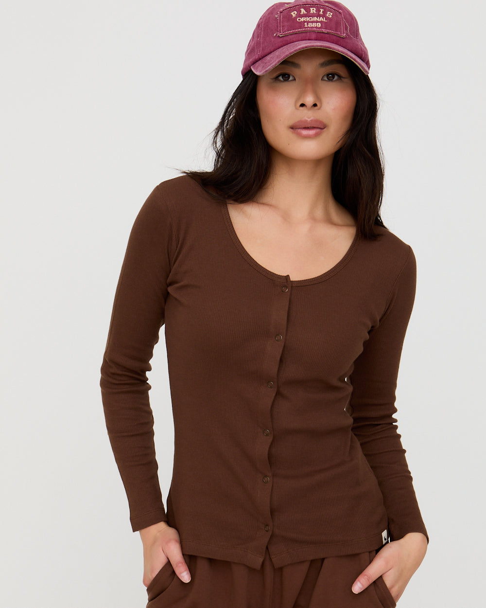 Woman wearing a brown long-sleeve top and matching pants with a maroon cap on a white background