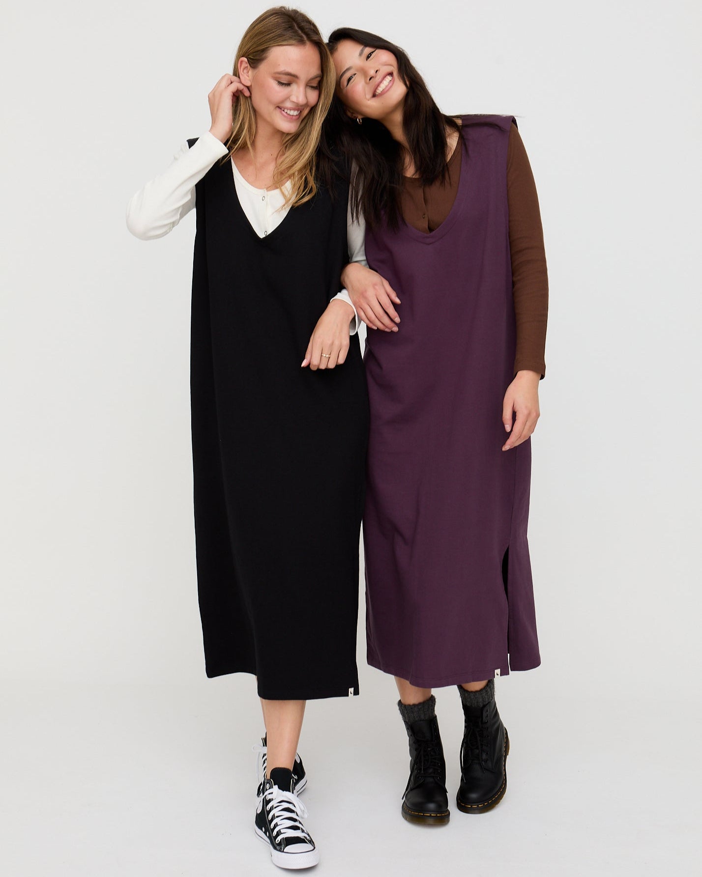 Two women wearing long dresses standing close together on a white background