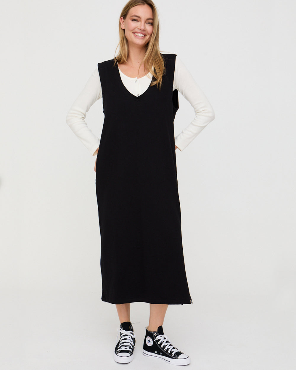 Woman wearing a black sleeveless dress over a white long-sleeve shirt on a white background