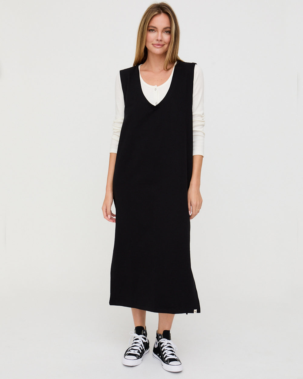 Woman wearing a black sleeveless dress over a white shirt on a white background