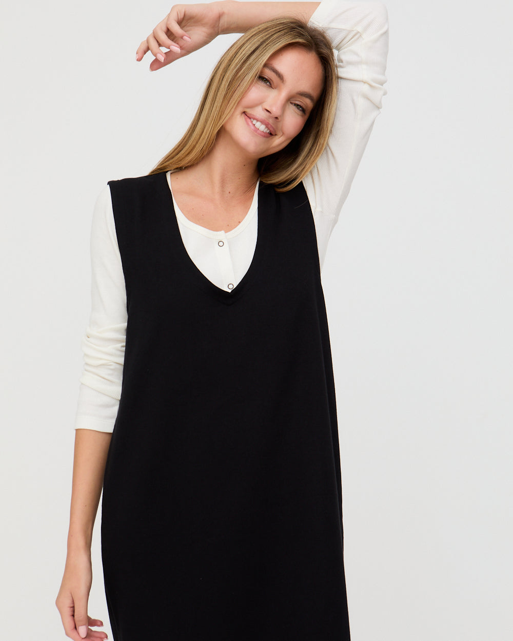 Woman wearing a black dress over a white shirt on a light gray background