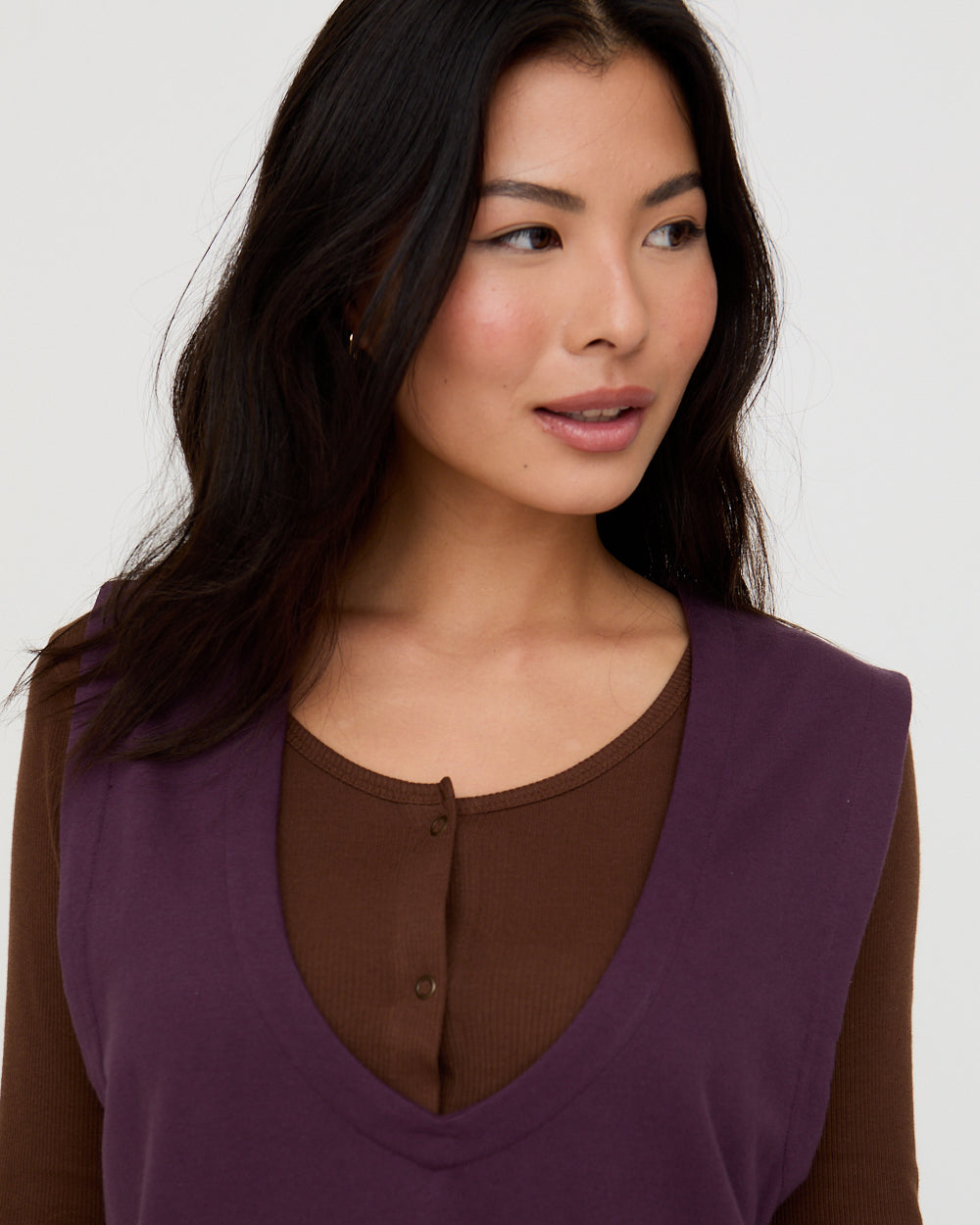 Woman wearing a purple top with a brown shirt underneath on a white background