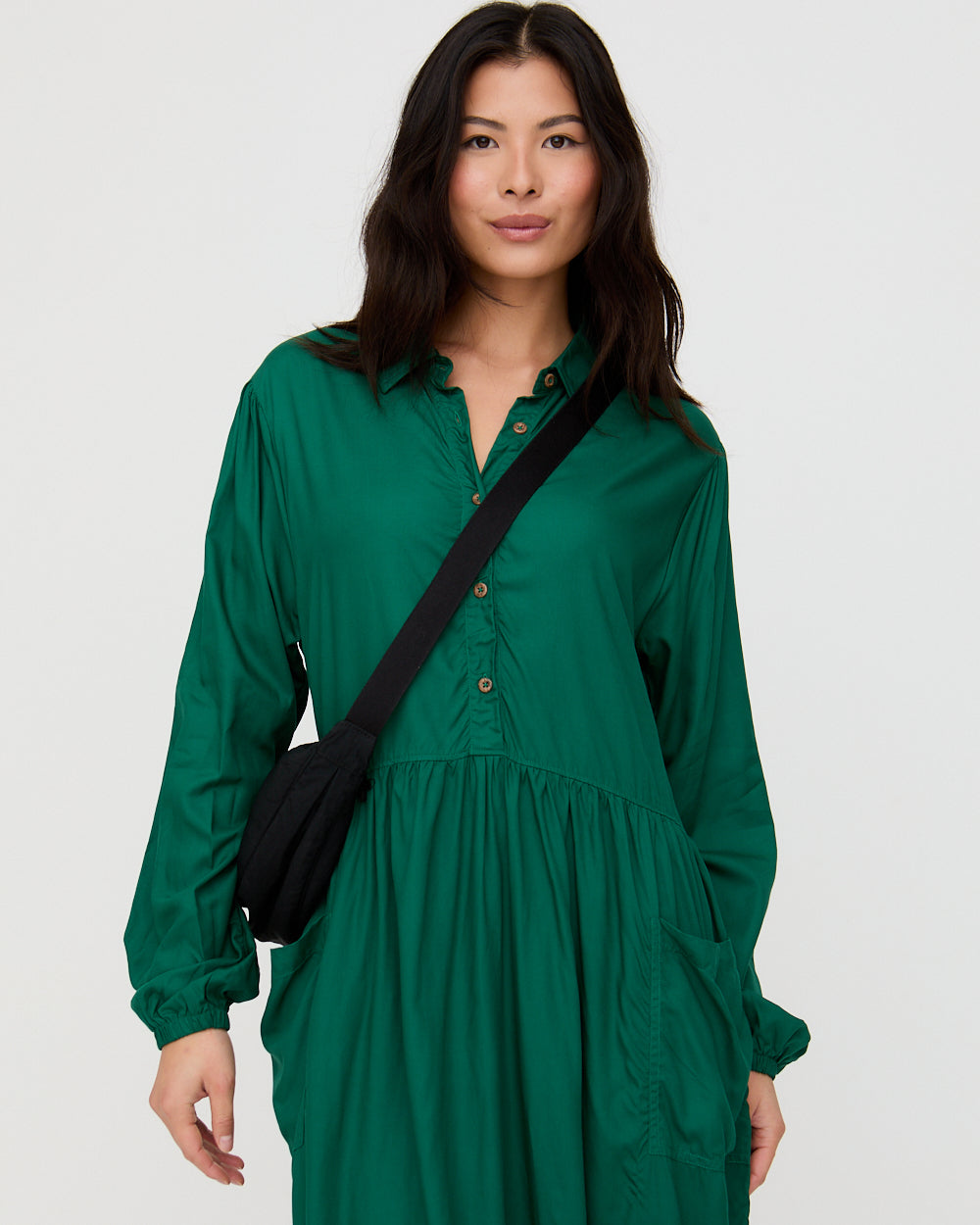 Woman wearing a green dress with a black crossbody bag on a white background