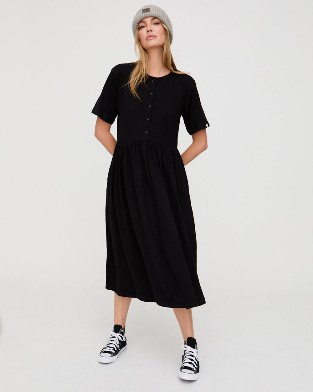 Woman wearing a black dress and black sneakers on a white background