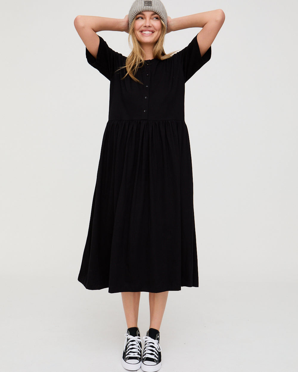 Woman wearing a black dress and black and white sneakers on a white background