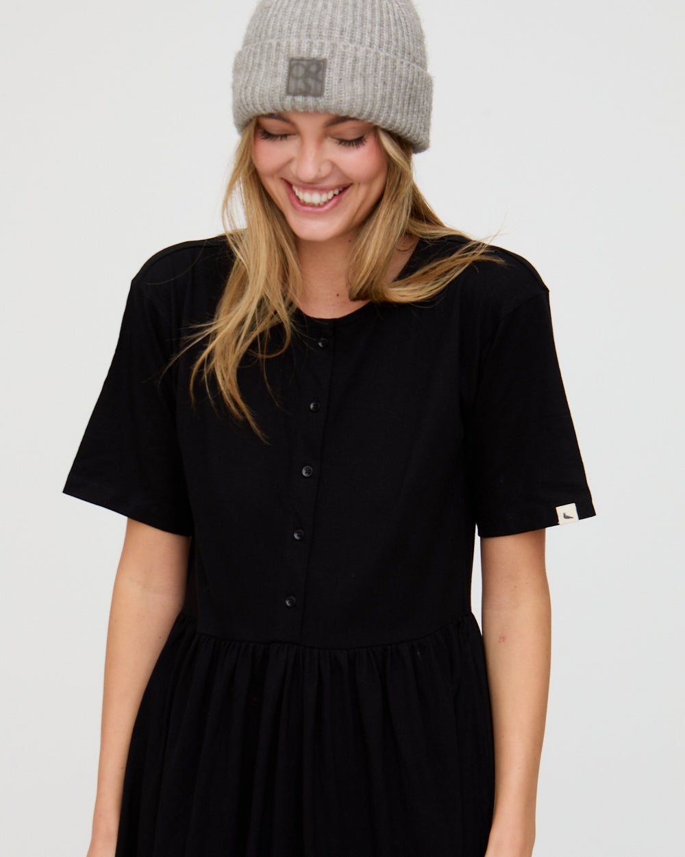 Woman wearing a black dress and gray beanie on a plain background
