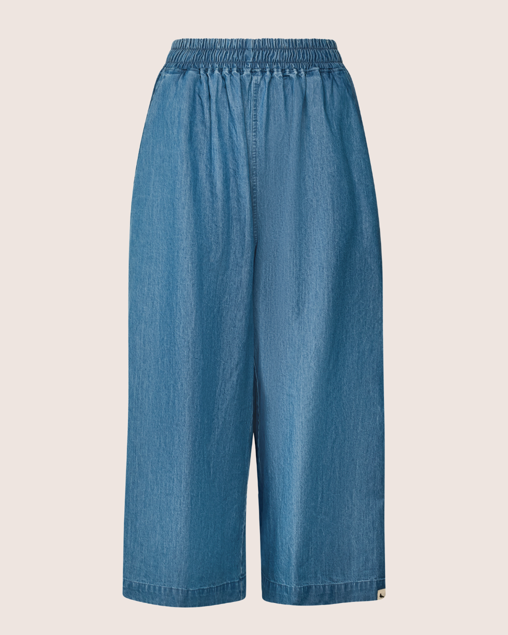 The Judy Washed Denim Blue Trousers, made from organic cotton, showcase an elasticated waistband, wide-leg style, and a cropped length. Photographed against a plain white background.