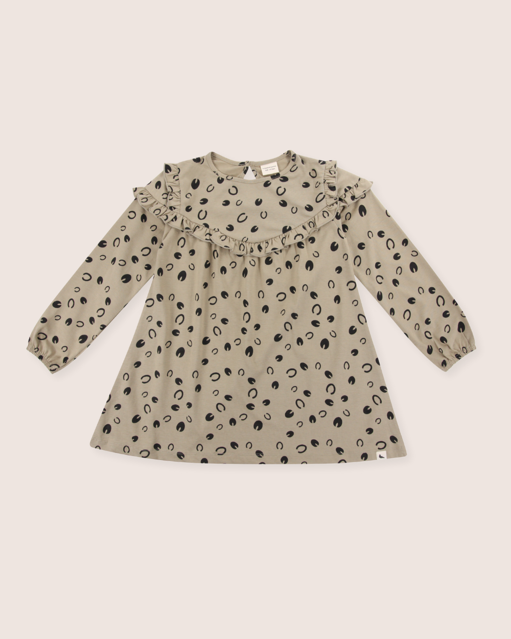 The Clip Clop Dress is a beige, long-sleeve A-line dress for children with black oval patterns. It ensures an Easy Fit for comfort, crafted from 100% GOTS organic cotton, and features a ruffled collar and cuffs with back buttons.