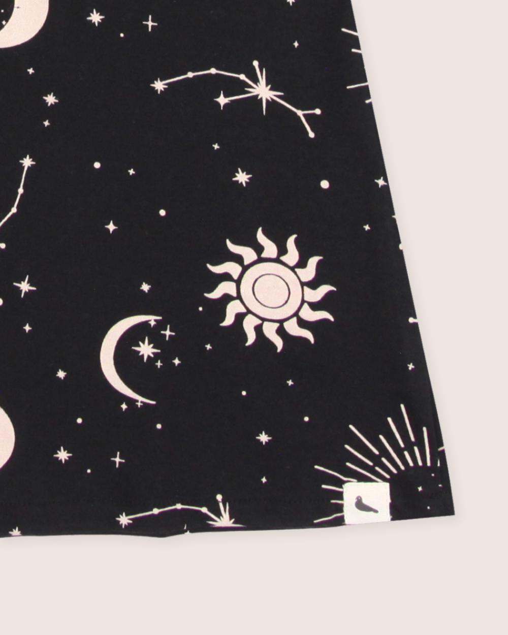 The Astrology Dress features an organic cord fabric with a celestial pattern of white outlines showcasing stars, crescent moons, constellations, and a sun design. Its ideal for kids dresses and is completed with a charming bird logo in the corner.