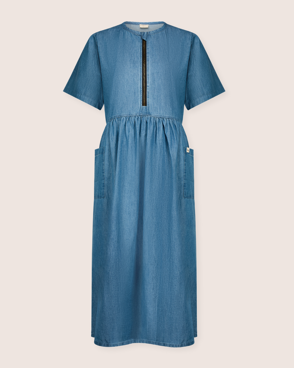 The Magda Washed Denim Blue Dress is a midi-length, casual shirt dress with short sleeves, a front zipper for easy breastfeeding access, gathered waist, and two large side pockets. Made from organic cotton in a simple design.