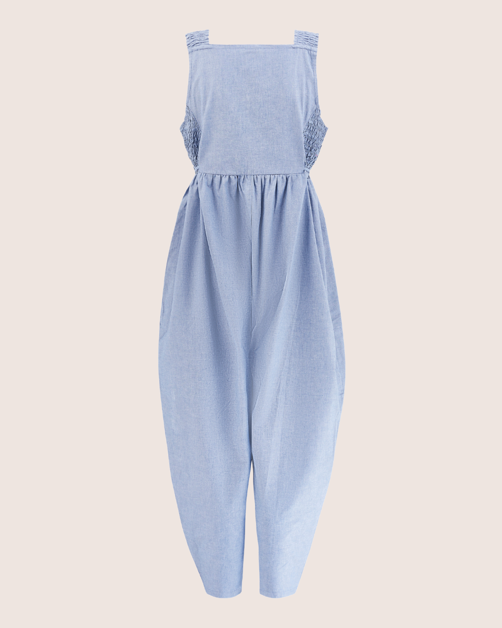 The Alice Chambray Dungarees are organic light blue sleeveless jumpsuits with a square neckline, gathered waist, wide tapered legs, and side textured fabric details against a light beige background.