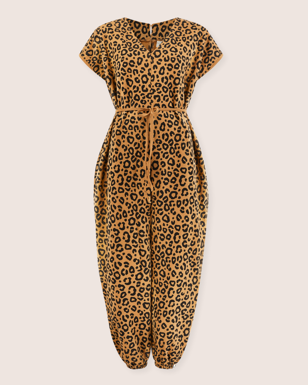 The Rita Tie Back Mini Animal Print Jumpsuit is made from organic cotton and features a V-neck and short sleeves. It has a cinched waist with a matching belt, loose-fitting legs gathered at the ankles with elastic hems, and boasts black and brown spots on a tan background.